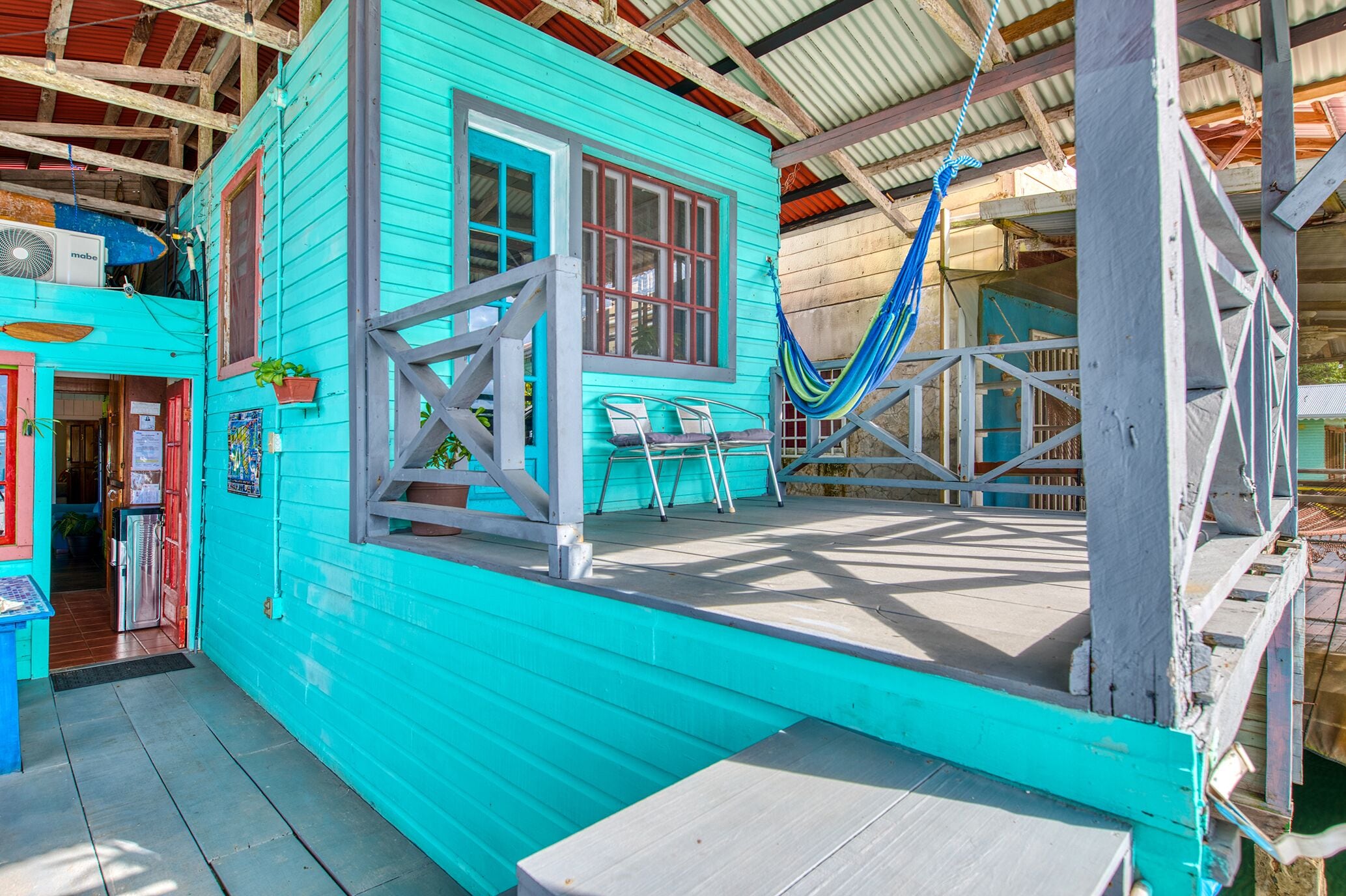 A turquoise building with a porch, a hammock, and a small table.