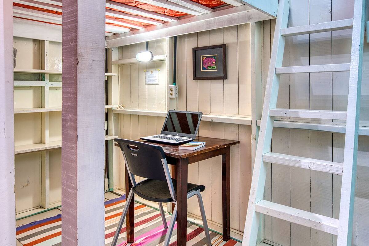 A bunk bed with a desk and chair, a ladder, and a striped rug in a room with wooden walls and a ceiling.
