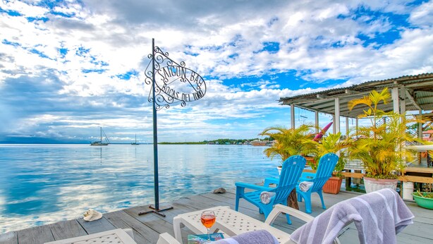 A wooden deck with lounge chairs, a sign reading "Alican Bay", and a view of the sea. - Saigon Bay Bed & Breakfast (Bocas del Toro)