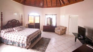 Ein Schlafzimmer mit Holzboden, einem großen Bett mit gemustertem Überwurf, einem Schminktisch, einem Stuhl, einem Fernseher und einem Teppich.