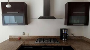 A kitchen with a gas stove, a coffee maker, and dark cabinets. - Casa Elena (Mazatlán)