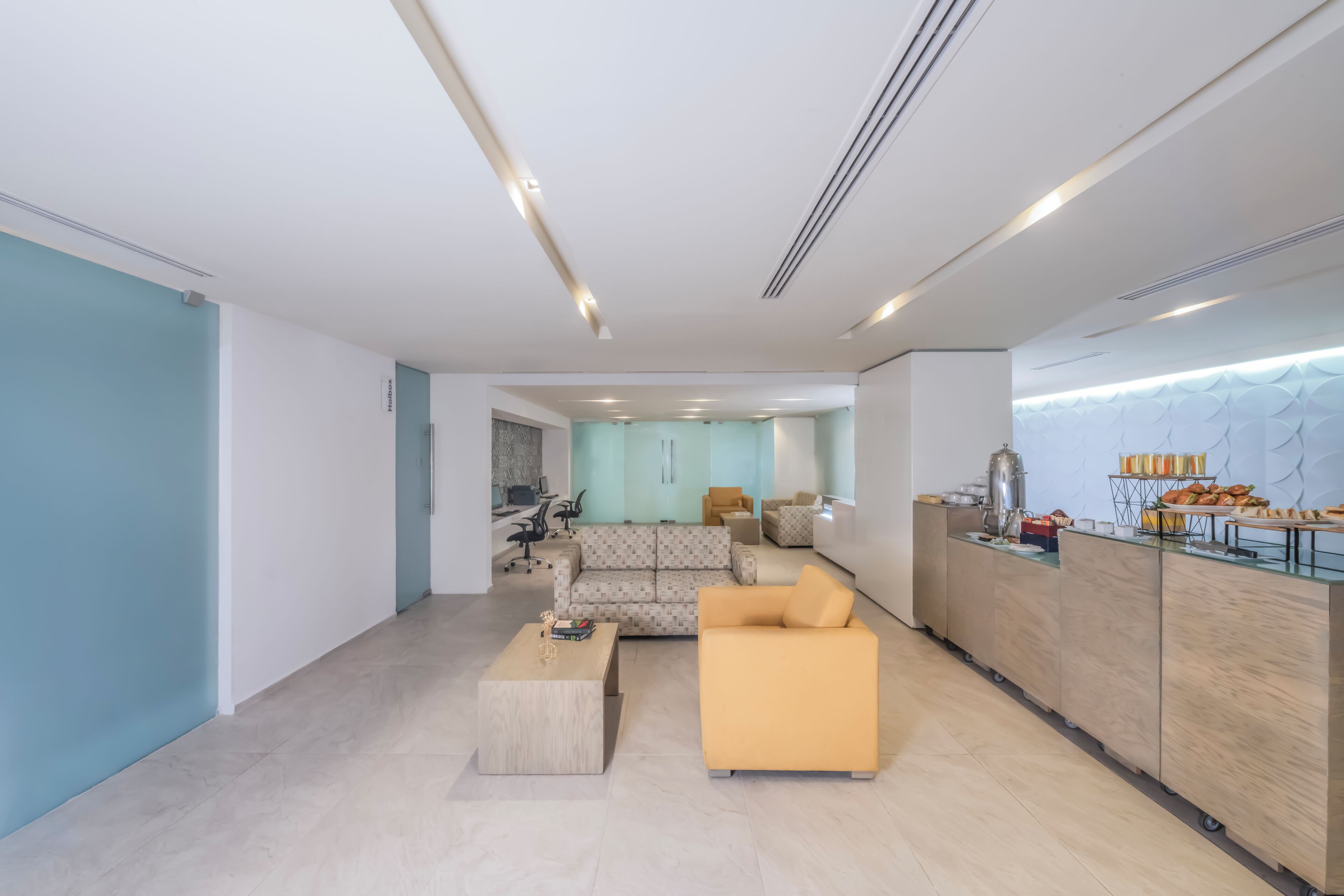 A modern hotel lobby with a sofa, coffee table, and a breakfast bar with pastries.