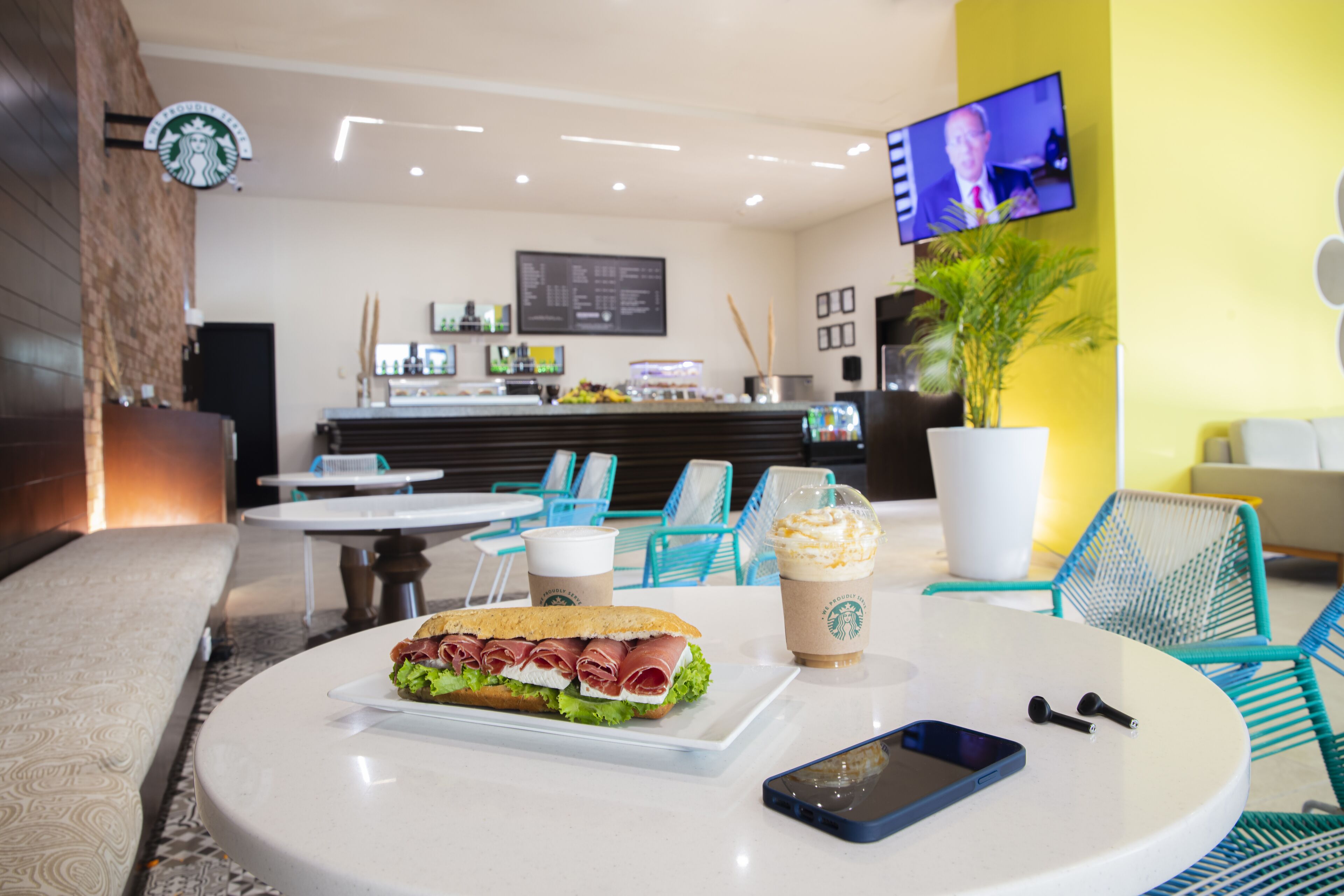 Una cafetería Starbucks con mesas, un sándwich, una bebida y un teléfono inteligente sobre la mesa.