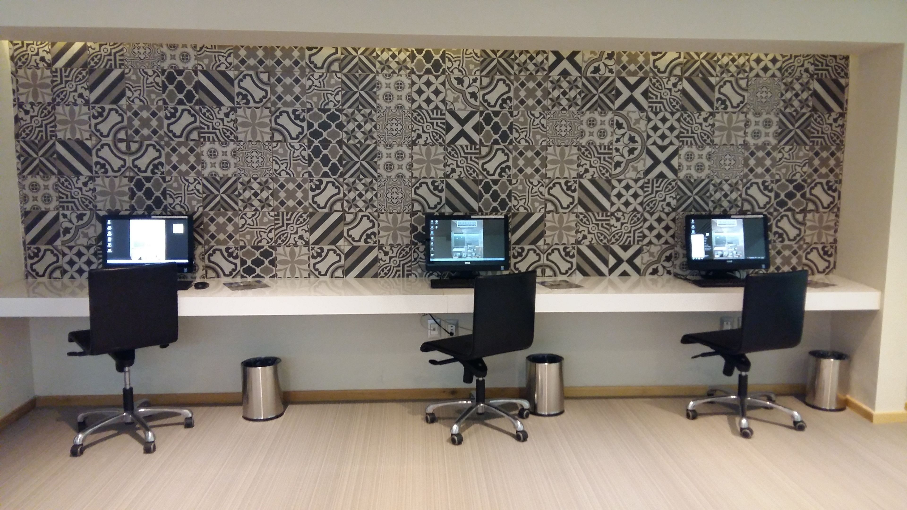 A workspace with three desks, each with a computer monitor, black office chairs, and a patterned wall in the background.