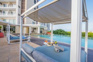 Un área de descanso junto a la piscina con una zona de estar cubierta, piscina y vistas de los edificios circundantes.