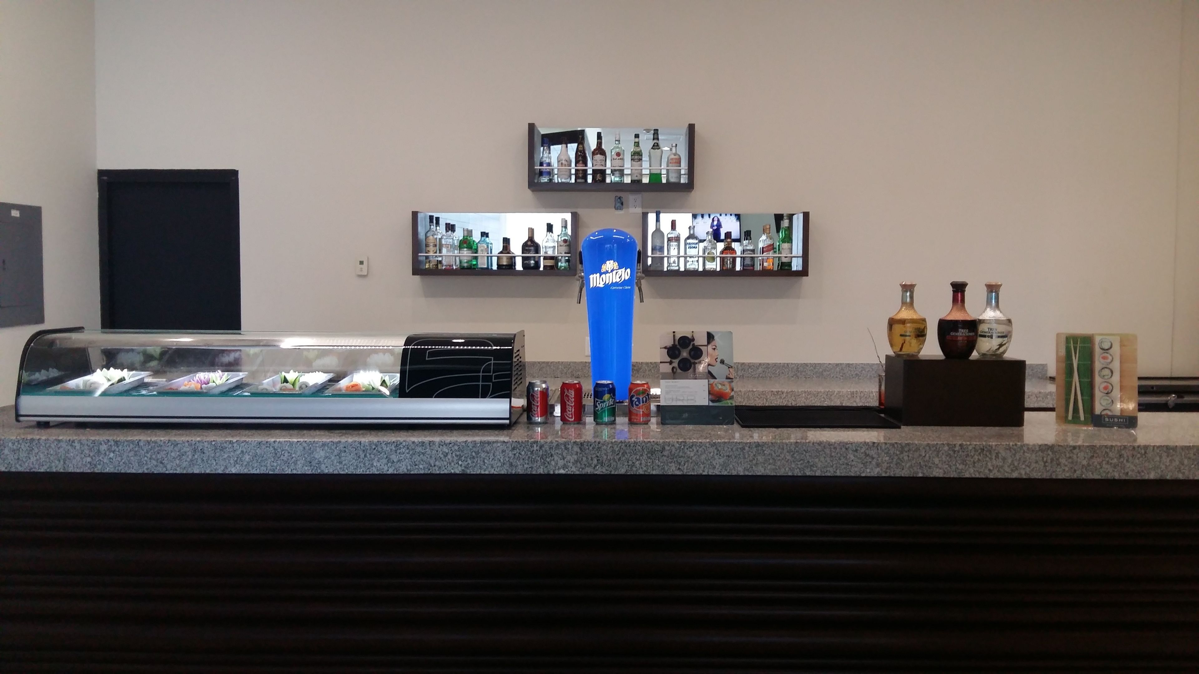 A hotel reception area with a display case of food items, a blue punch bowl, and shelves with liquor bottles.