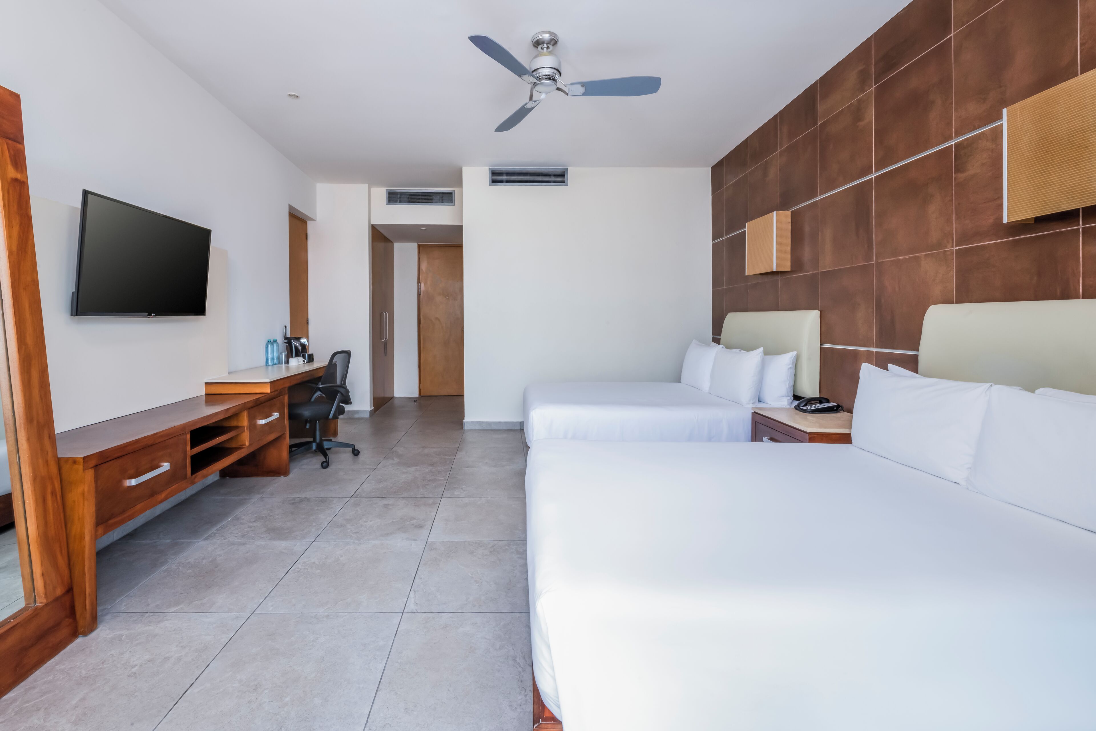 Una habitación de hotel con un escritorio de madera, un televisor de pantalla plana, una cama y un ventilador de techo.
