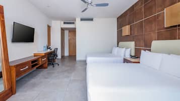 A hotel room with a wooden desk, a flat-screen TV, a bed, and a ceiling fan.