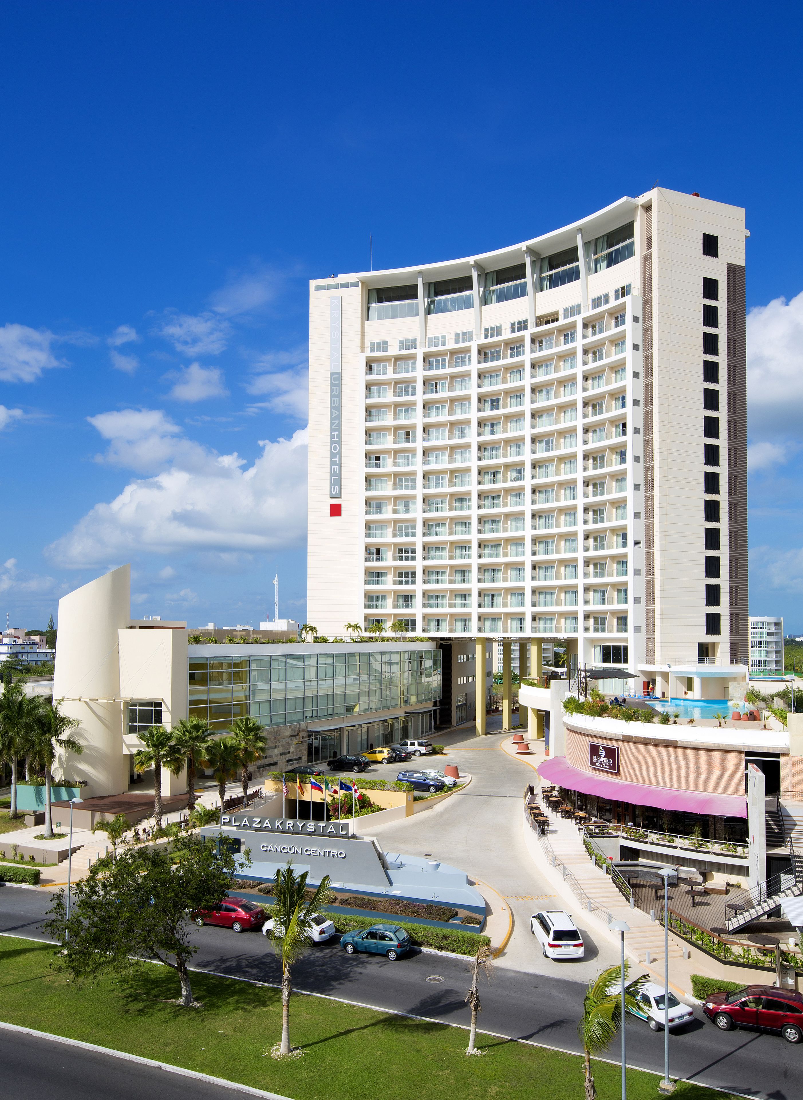 A multi-story hotel with a modern design, featuring a central atrium and a parking area with several cars.