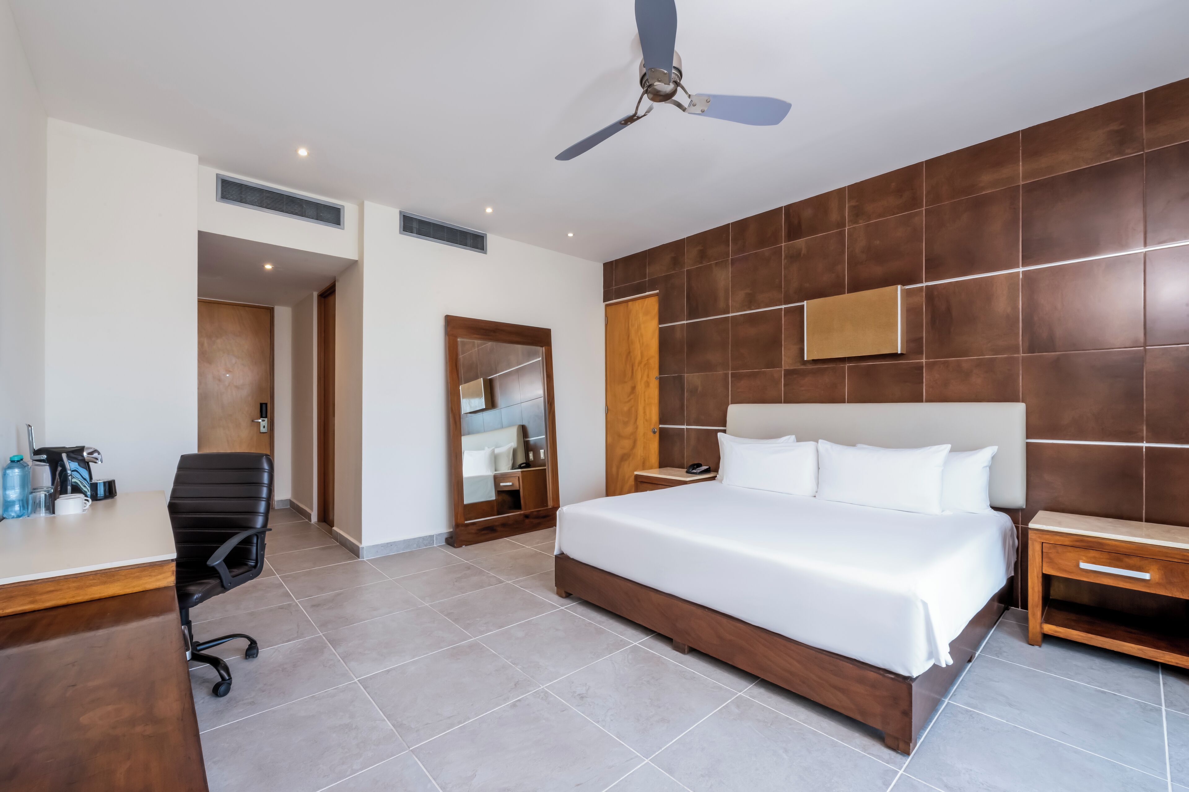 A modern hotel room with a large bed, a desk with a chair, a ceiling fan, and a wooden accent wall.