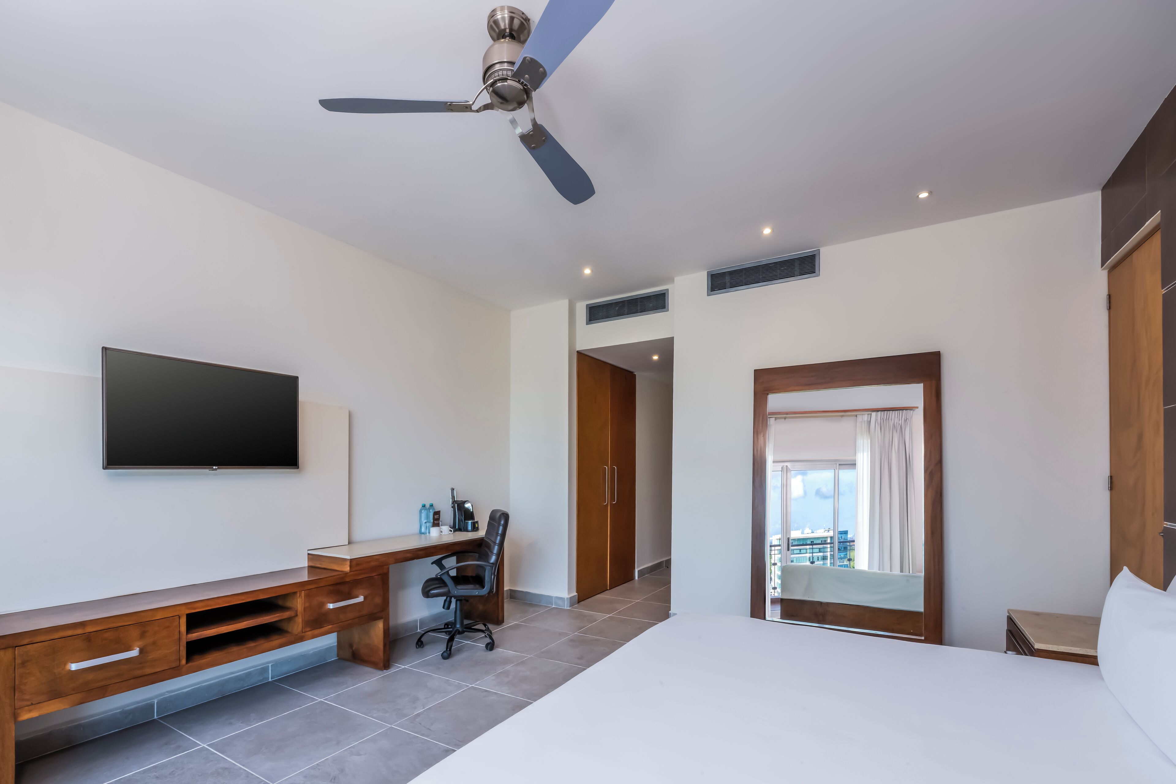 Una camera d'albergo moderna con un letto, una scrivania, una sedia, un televisore, un armadio e una ventola a soffitto.