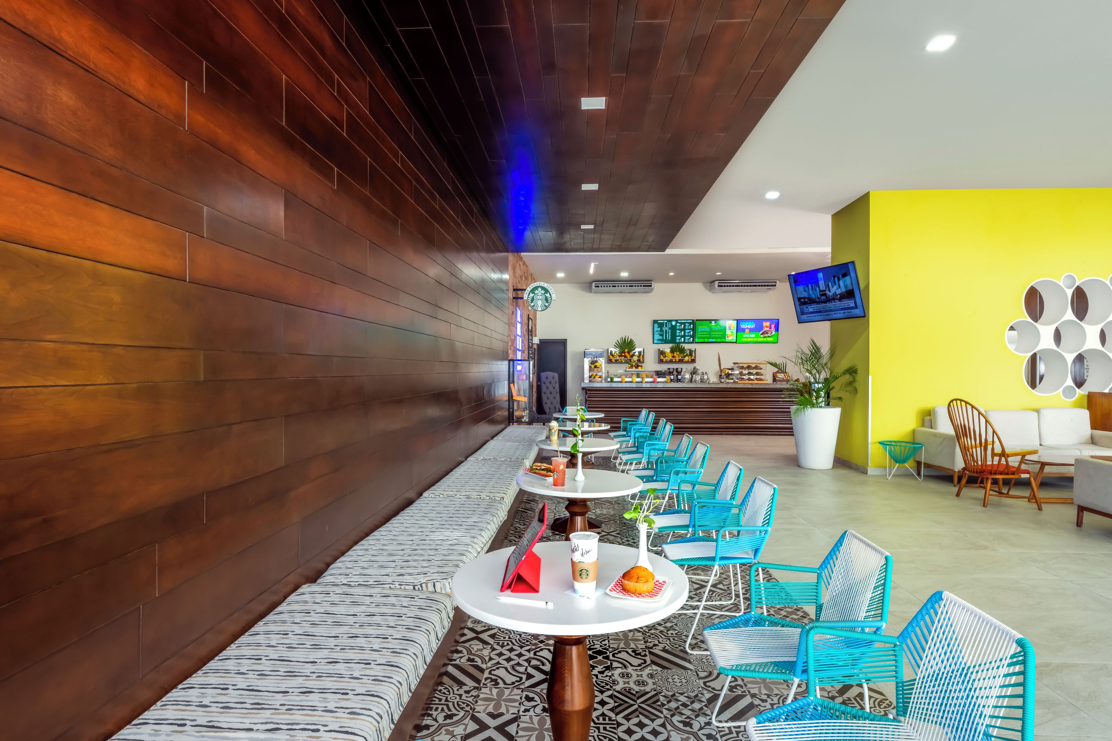 A modern interior with wooden paneling, a seating area with tables and chairs, a bar, and a TV screen.