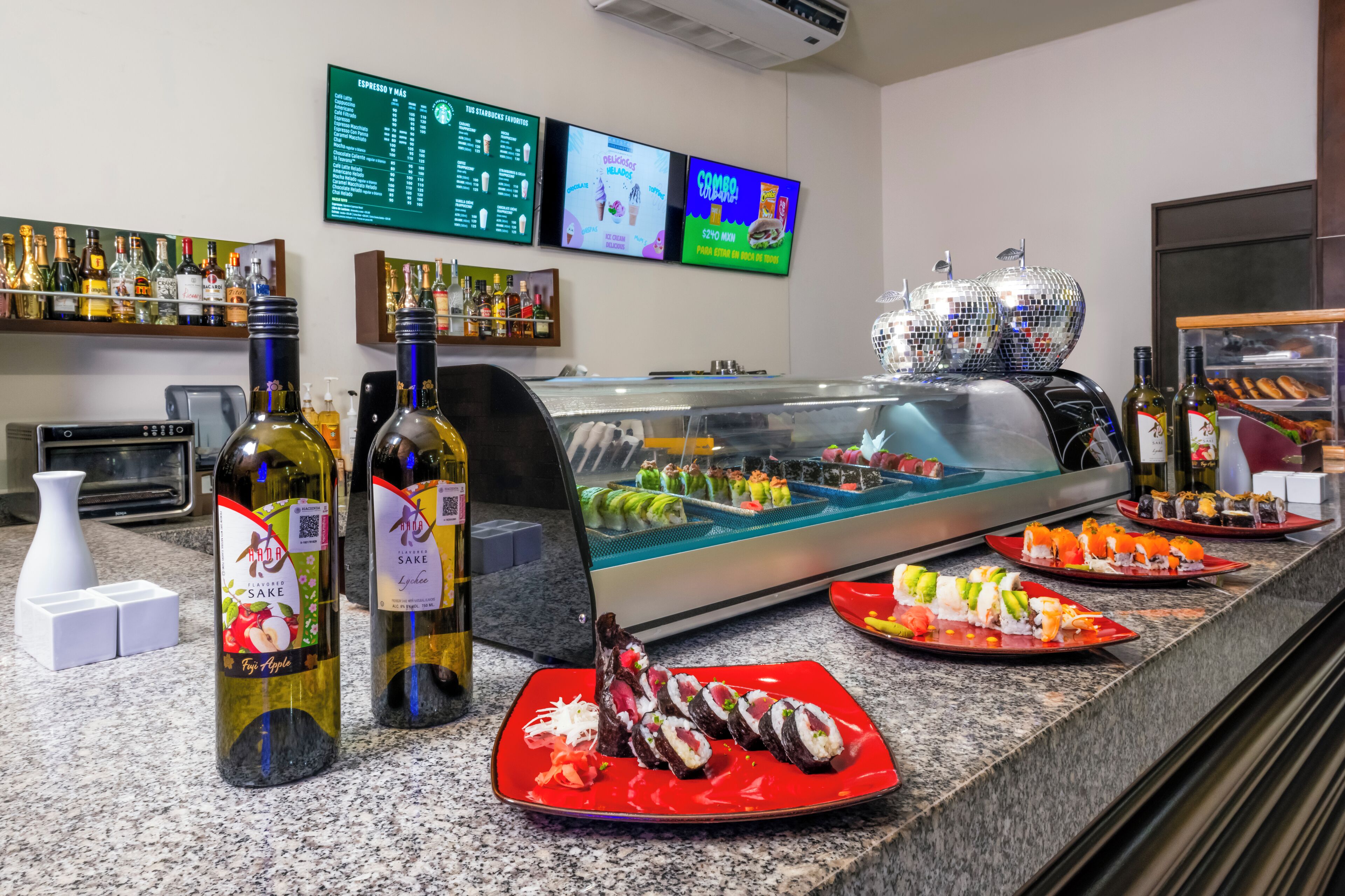 Un bar de sushi con diversas opciones de platos, incluyendo rollos de sushi y sashimi, además de una selección de botellas de vino.