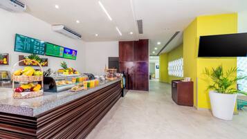 A modern hotel reception area with a fruit display, digital menu boards, and a bright yellow accent wall.