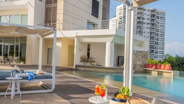 A modern hotel pool area with a covered seating area, lounge chairs, and a dining setup. - Krystal Urban Cancun & Beach Club (Cancun)