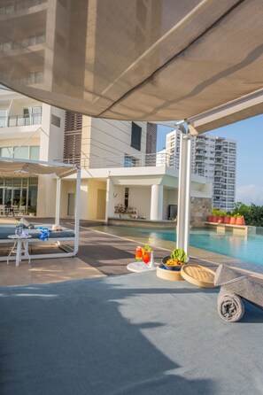 A modern hotel pool area with a covered seating area, lounge chairs, and a dining setup. - Krystal Urban Cancun & Beach Club (Cancun)