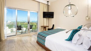 A hotel room with a large bed, a TV mounted on the wall, a balcony with a chair, and a view of the city. - Krystal Urban Cancun & Beach Club (Cancun)
