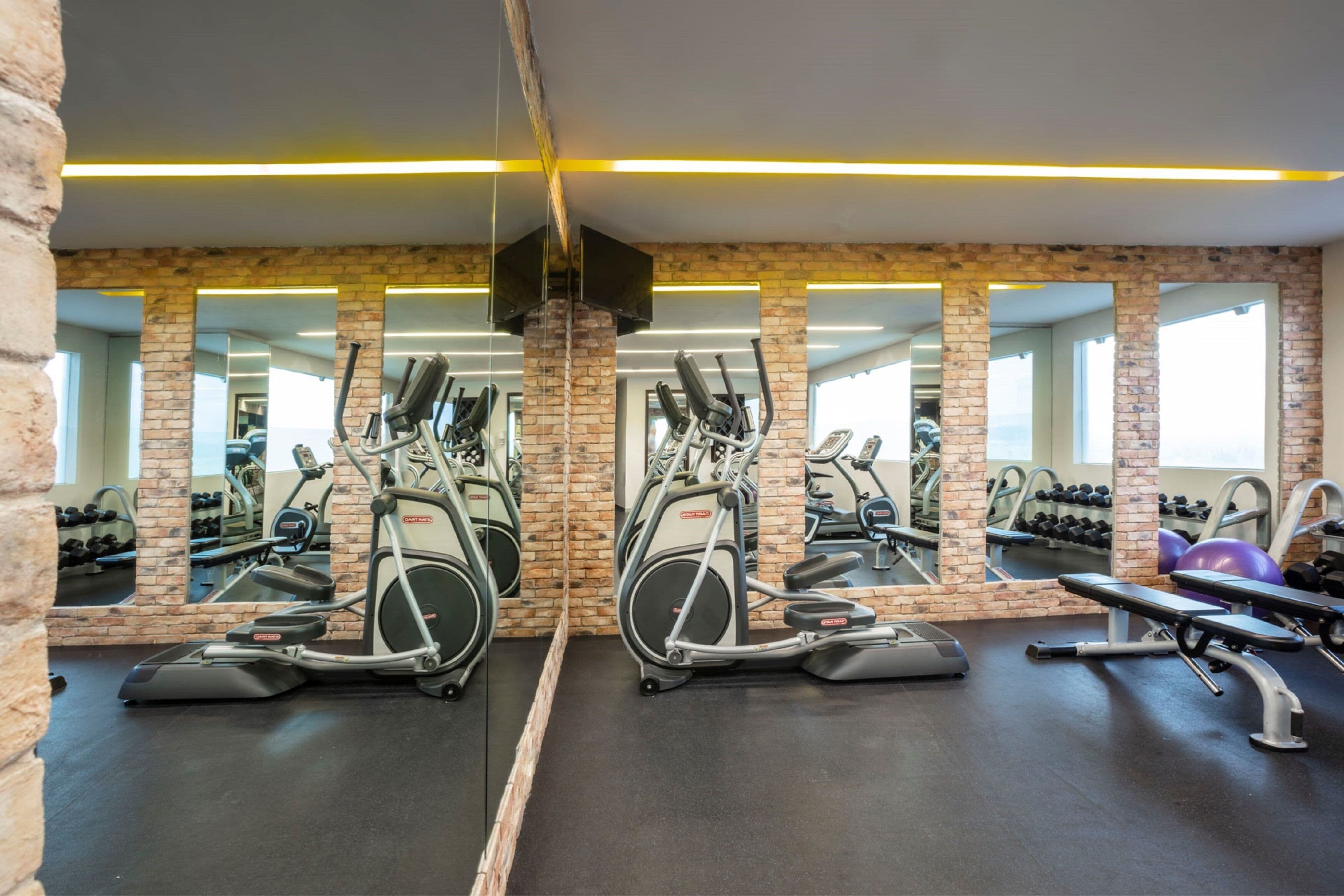 Een sportschool met spiegelwanden, trainingsapparatuur en een met baksteen beklede muur.