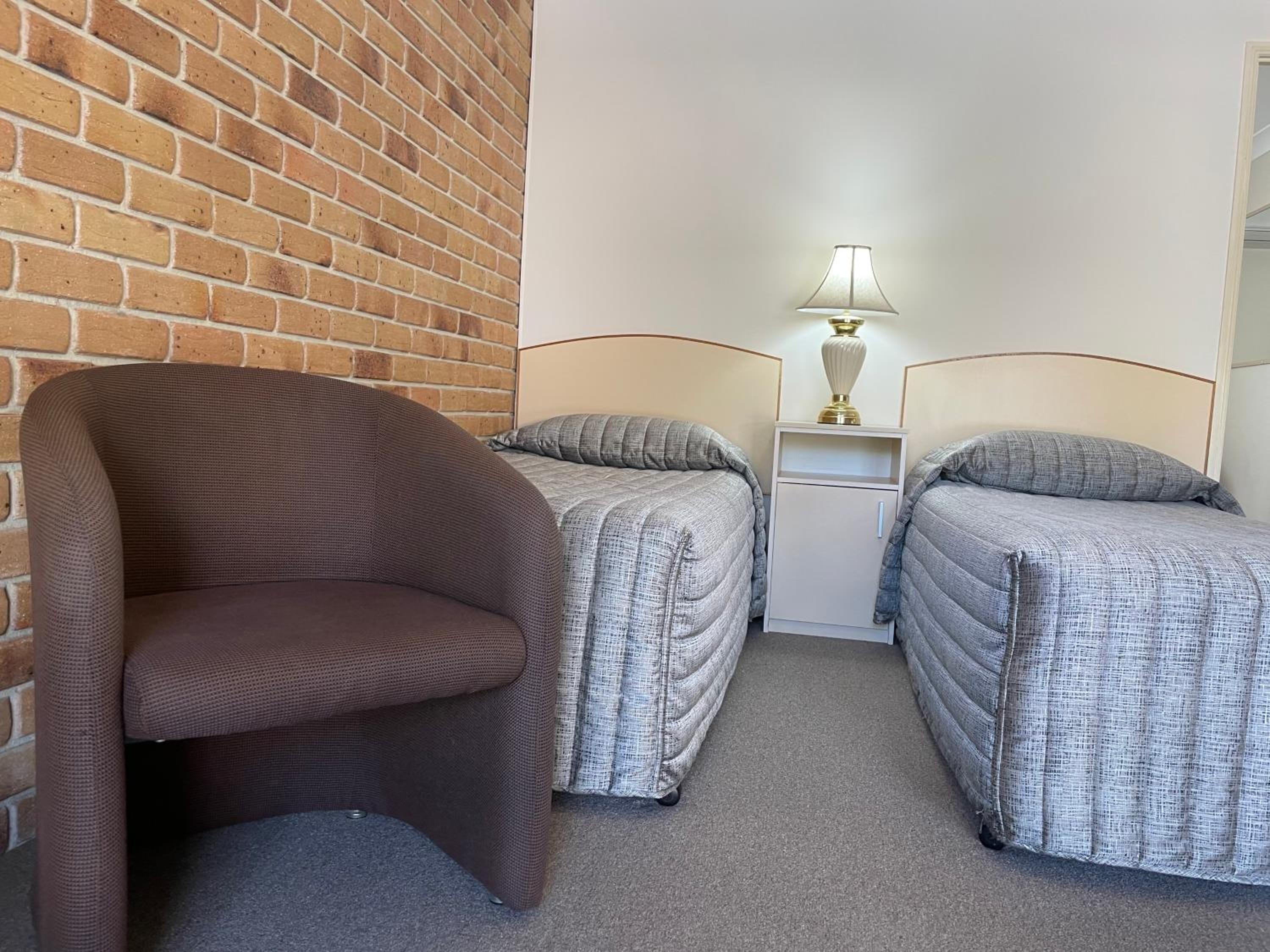 A room with two beds, a chair, and a nightstand with a lamp.