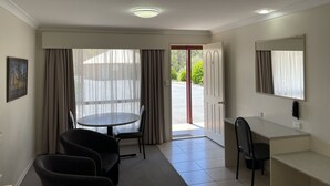 A hotel room with a dining table, two chairs, a desk with a chair, a mirror, and a door leading outside.