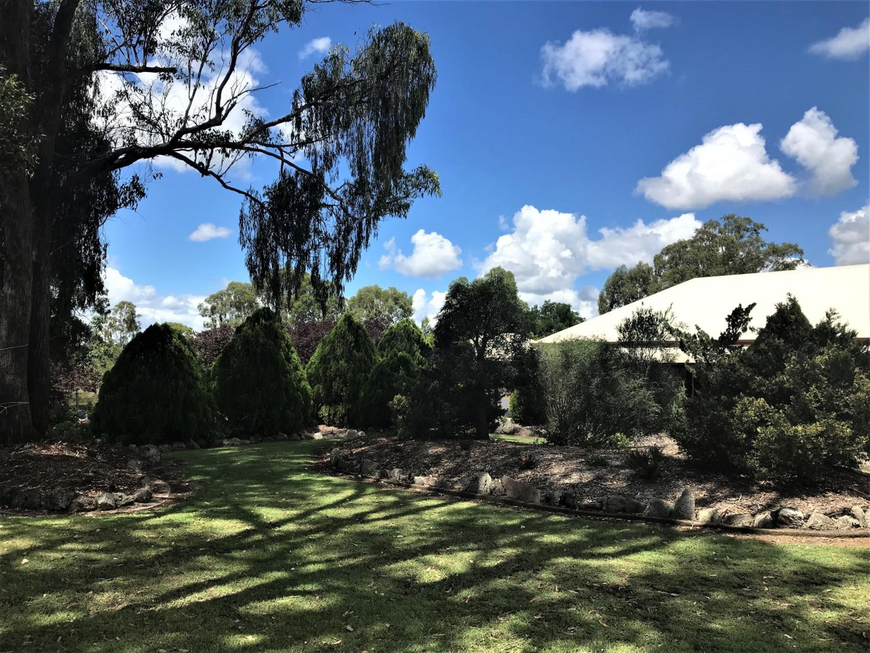 A well-maintained garden with various trees and shrubs, a grassy lawn, and a stone pathway.