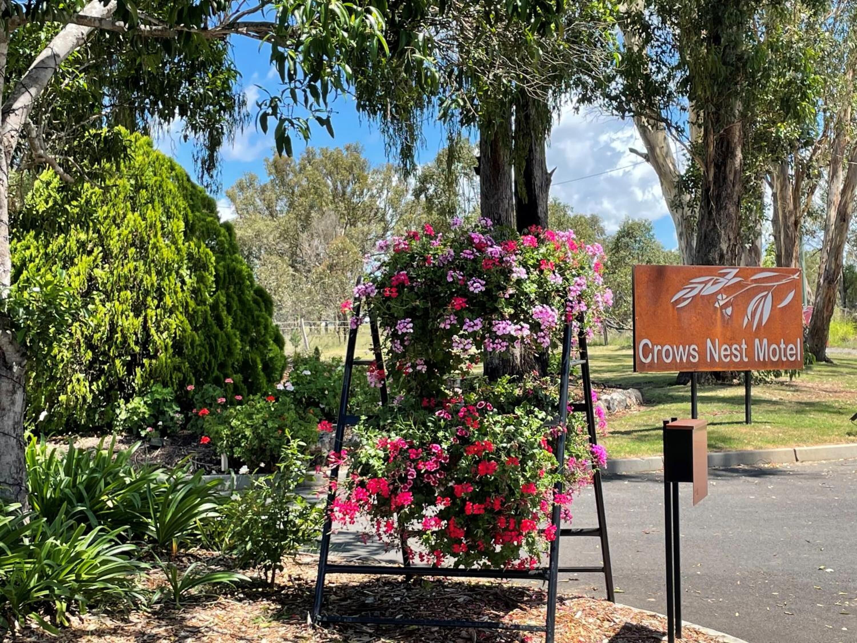 A sign for Crows Nest Motel with a metal structure supporting pink flowers.