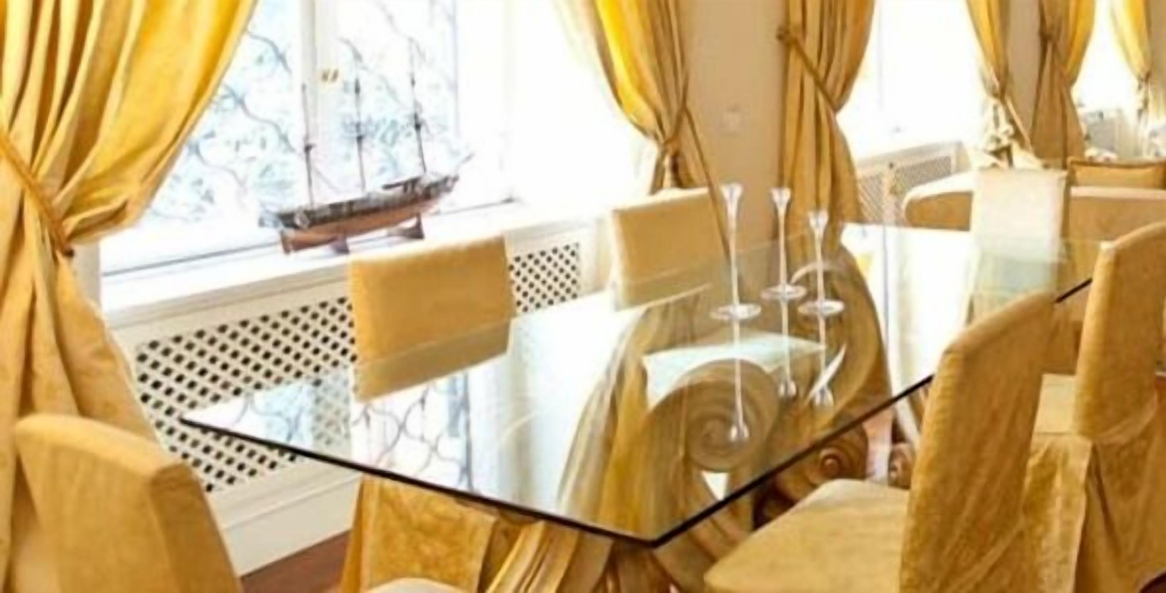 A room with a glass table, yellow curtains, and a ship model on the window sill.