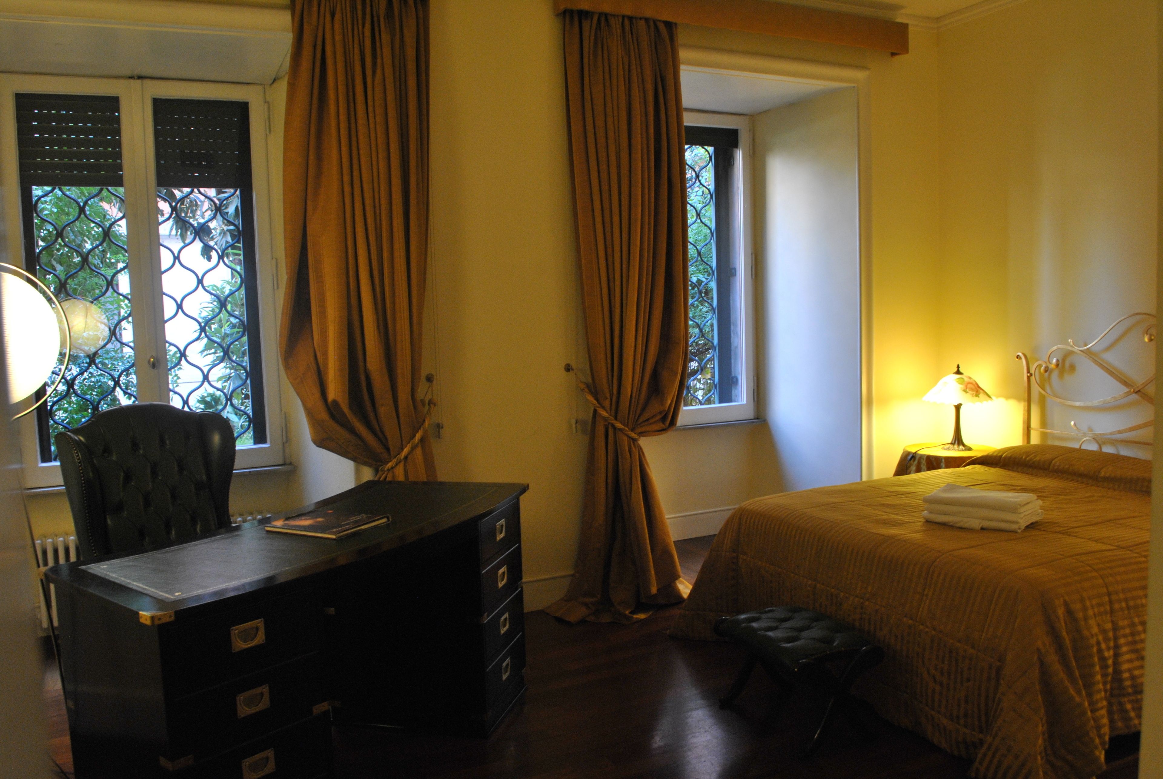 Habitación de hotel con escritorio, silla, cama y ventana con cortinas.