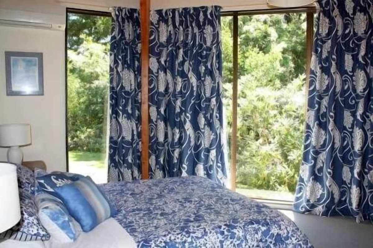 A bedroom with a large window, a bed with patterned bedding, and curtains with a leaf design.