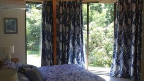 A bedroom with a bed, a window with curtains, and a view of greenery outside.