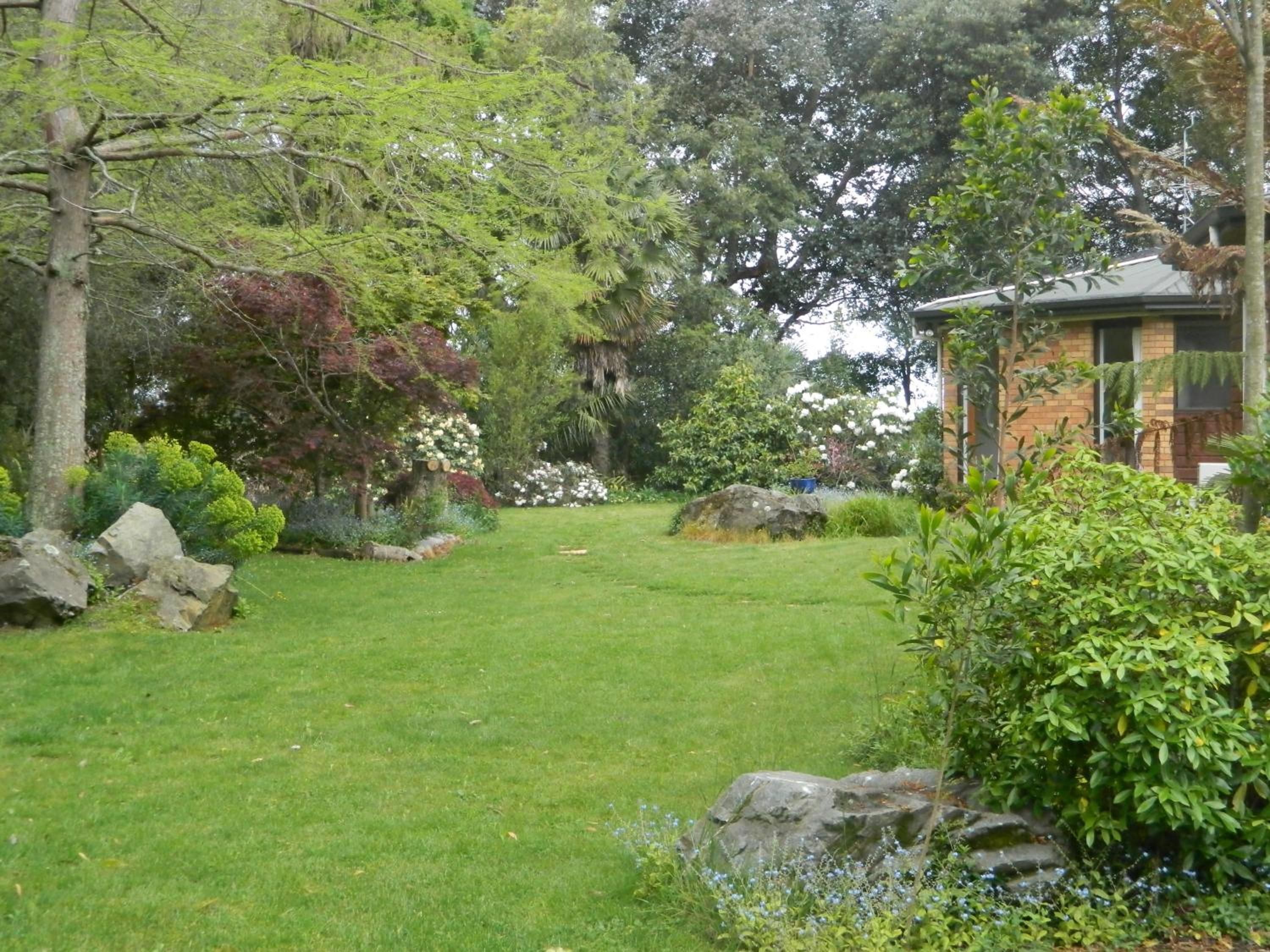 Un jardin bien entretenu, avec une variété de plantes et d’arbres, une pelouse verdoyante et un bâtiment en briques en arrière-plan.