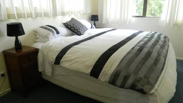 Een slaapkamer met een bed, nachtkastje, lamp en een raam met gordijnen.
