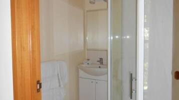 Un bany amb una cabina de dutxa de vidre, un lavabo amb mirall i una porta de fusta.