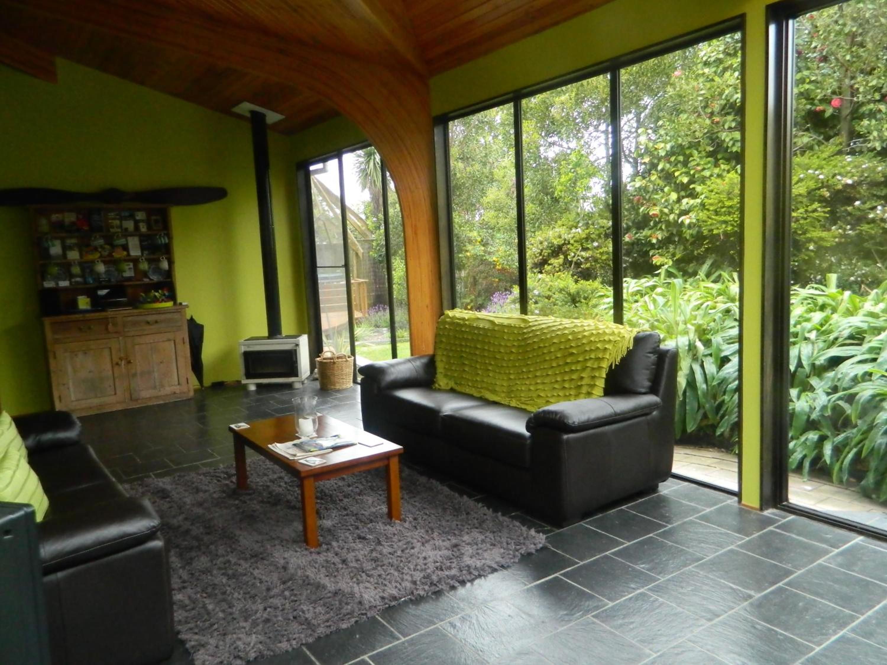 Un salon moderne avec un canapé en cuir noir, une table basse en bois et un tapis à poils longs gris. On aperçoit un petit meuble en bois et une cheminée à l’arrière-plan.