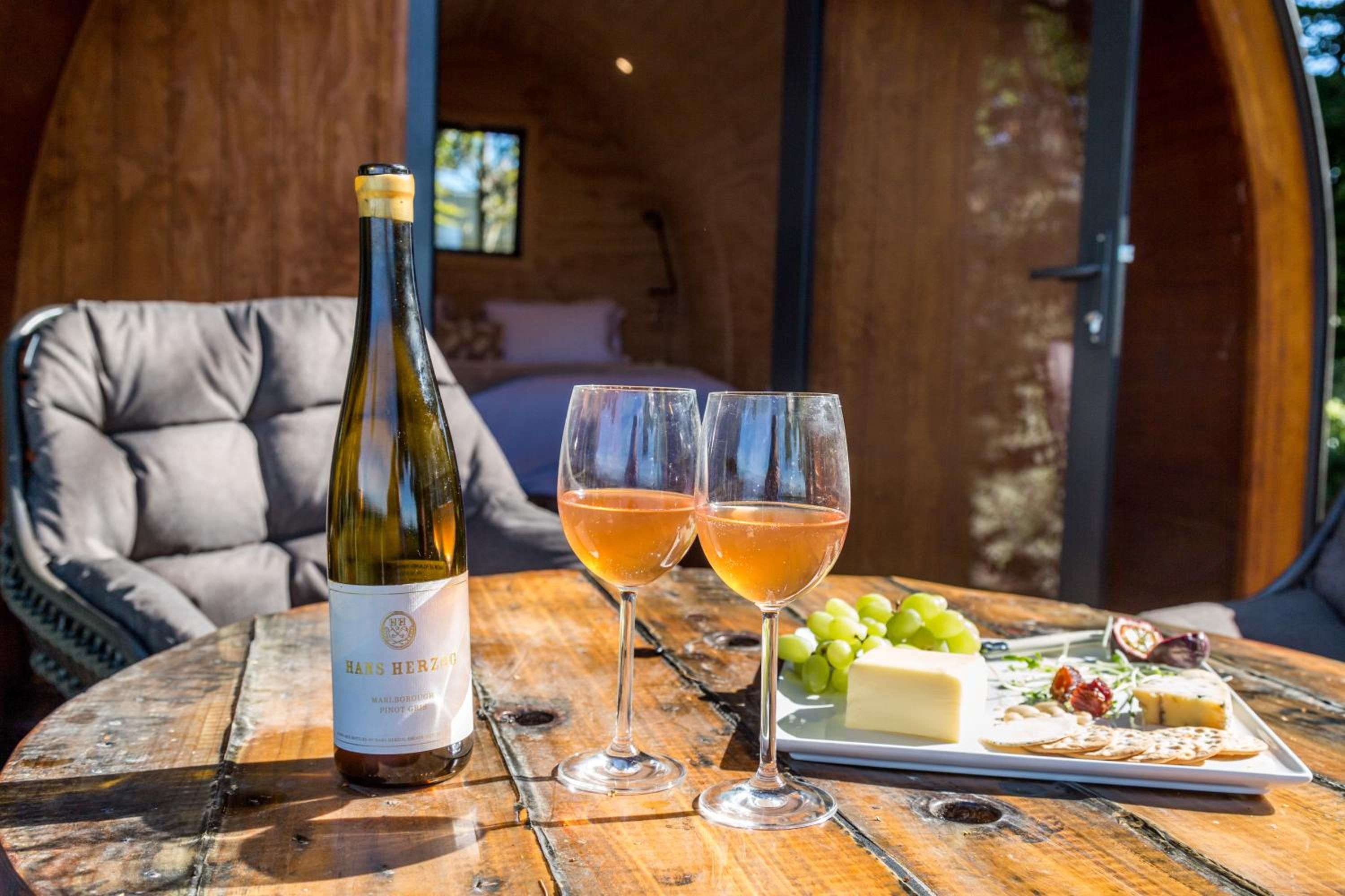 Una bottiglia di vino, due bicchieri di vino, un piatto con formaggio e uva, e un'area salotto accogliente con vista sull'esterno.