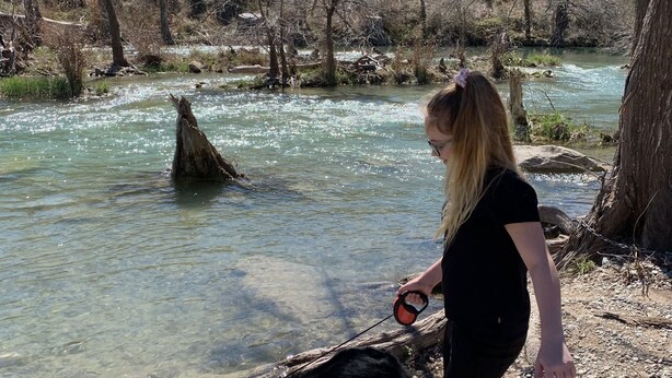 A person walking a dog along a riverbank with clear water and a natural, wooded backdrop. - The Blanco River is calling your name!! Come and enjoy!! (Wimberley)
