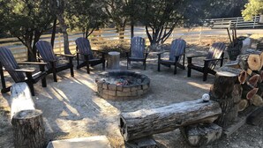 A fire pit surrounded by Adirondack chairs, a stone fire ring, and a log firewood stack. - The Blanco River is calling your name!! Come and enjoy!! (Wimberley)