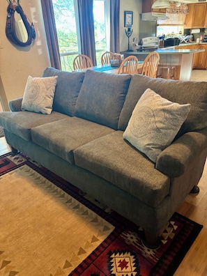 A grey sofa with patterned cushions, a patterned rug, and a kitchen in the background.