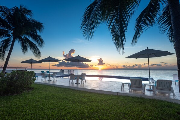 Zona junto a la piscina con sillas y sombrillas, con vista al mar al atardecer.