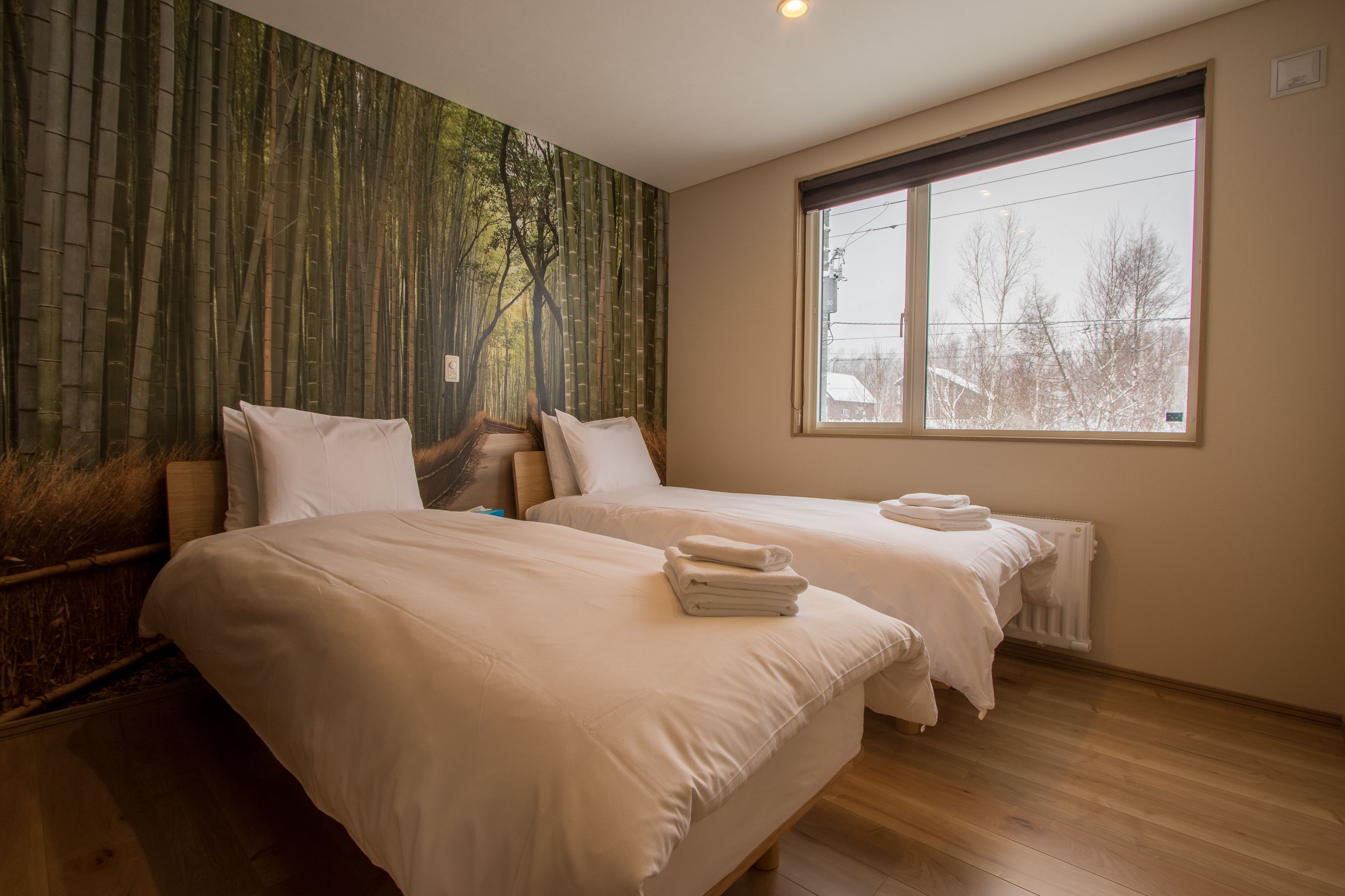 A hotel room with two beds, a large window, and a bamboo forest mural on the wall.