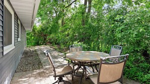 Une terrasse extérieure avec une table ronde et des chaises, entourée d’une végétation luxuriante et d’arbres.