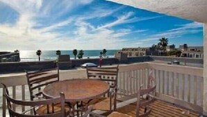 Terraço com vista para o mar e edifícios, com mobiliário de madeira e guarda-corpo.
