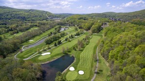 Vista aérea de un campo de golf con varios hoyos, cuerpos de agua y colinas boscosas circundantes.
