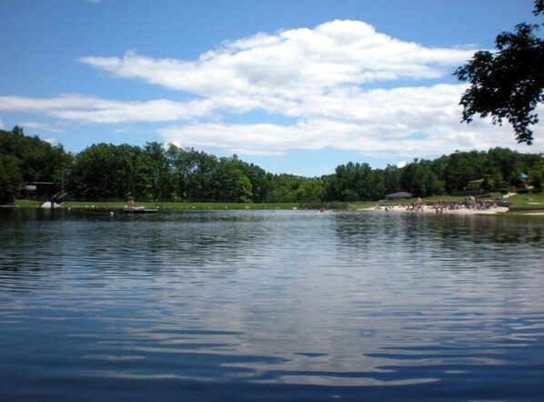 Un lago tranquilo con una playa arenosa y árboles al fondo.