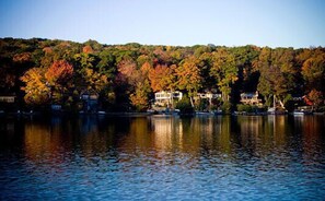 Une vue sur le lac, avec les couleurs automnales des arbres, un quai et des bâtiments le long de la rive.