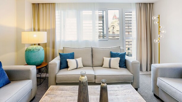 A modern hotel room with a sofa set, a lamp, decorative vases, and a view of a building through the window.