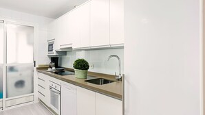 A modern kitchen with white cabinetry, a stainless steel sink, a coffee maker, and a potted plant.