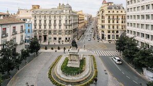 A city square with a central fountain, surrounded by historic buildings with classical architecture.
