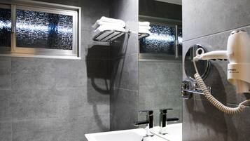 A modern bathroom with a large mirror, a white sink, a hairdryer mounted on the wall, and a towel rack.