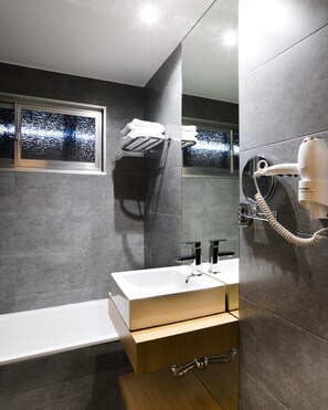 A modern bathroom with a large mirror, a white sink, a hairdryer mounted on the wall, and a towel rack.